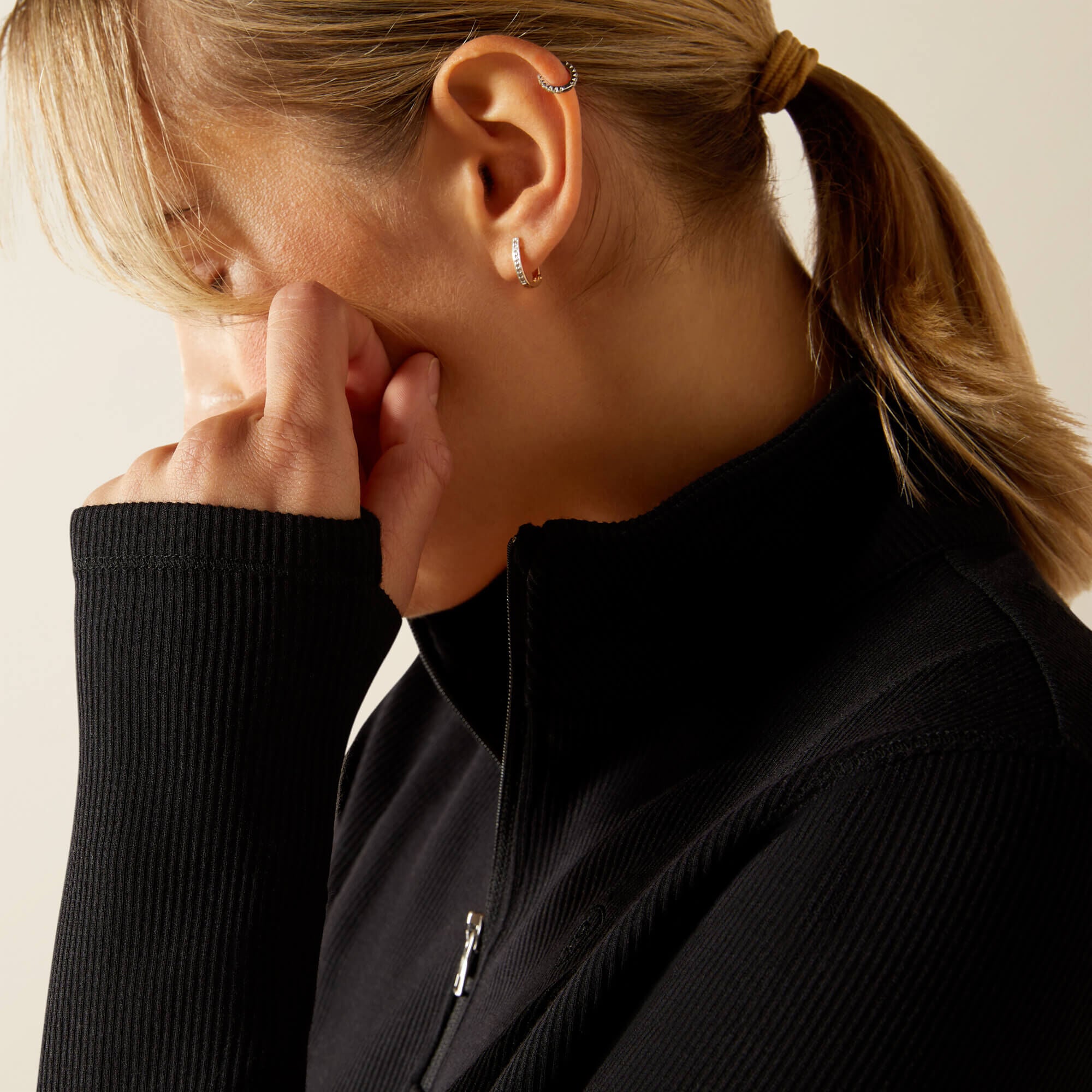 Woman wearing a black Ariat Lucent long sleeve, quarter zip baselayer with a neutral background