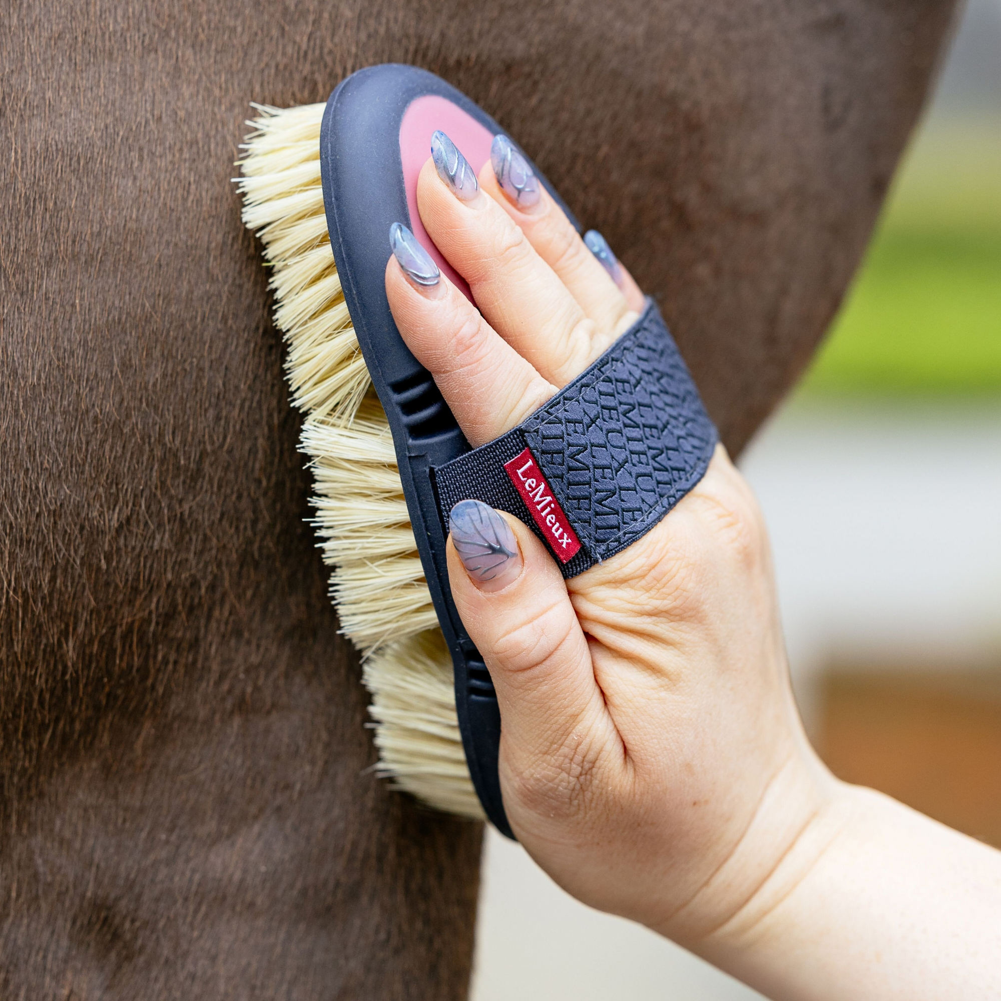 Lifestyle image of a woman brushing a horse with LeMieux&