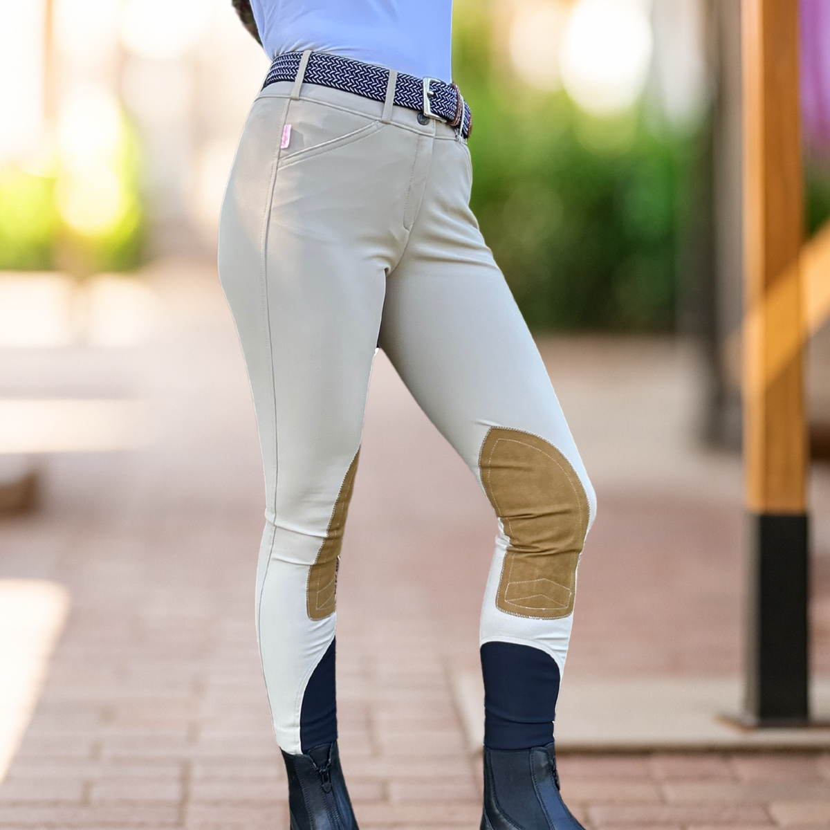 A rider wearing beige Tailored Sportsman knee patch riding breeches with a low-rise waist and front zip and boot socks, featuring clarino suede patches on the knees.