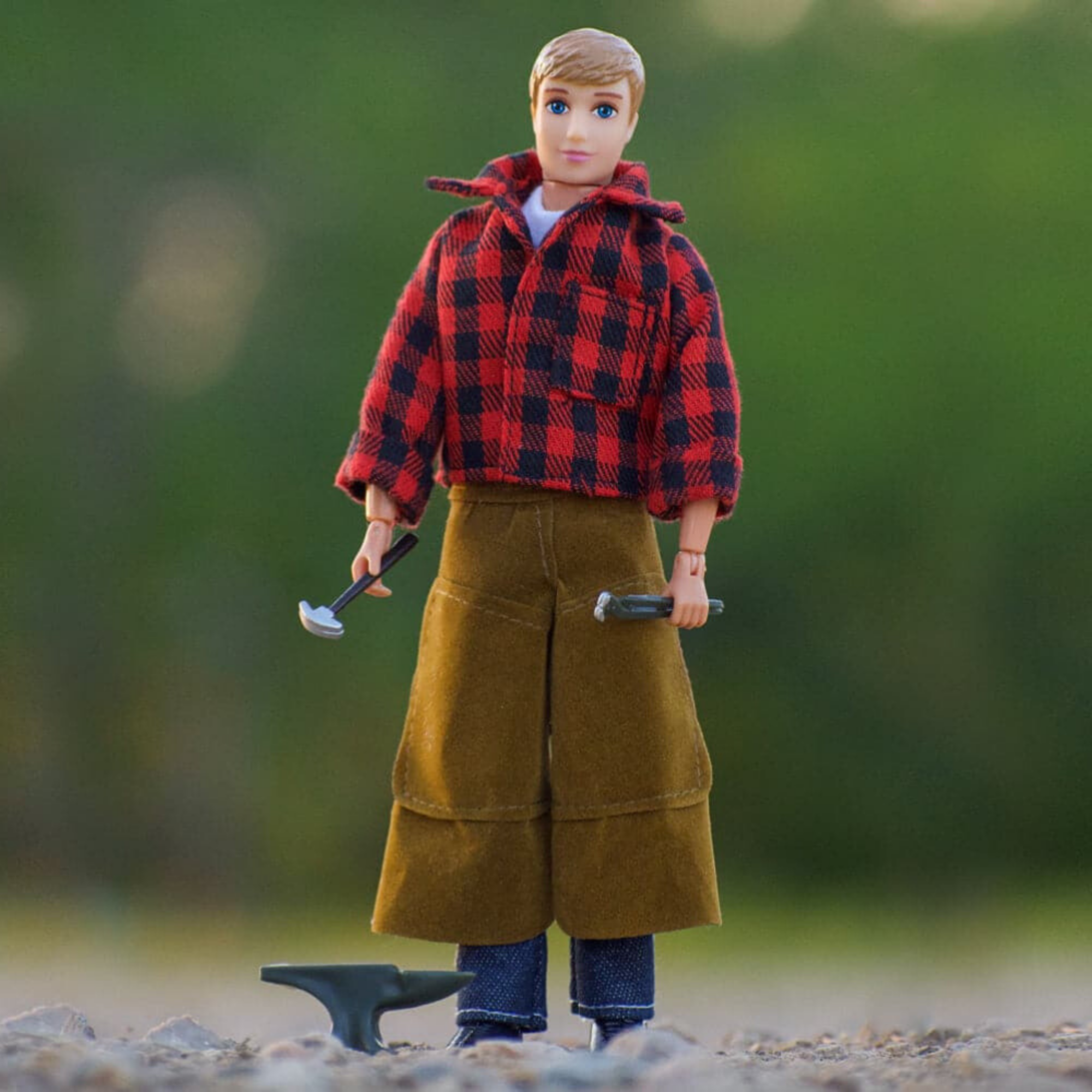 An articulated 8-inch Breyer Horse farrier figure with blacksmith tools, wearing a red and black checkered shirt, brown pants, and a black hat. The figure is equipped with a set of horseshoes and is holding a hammer and a file.