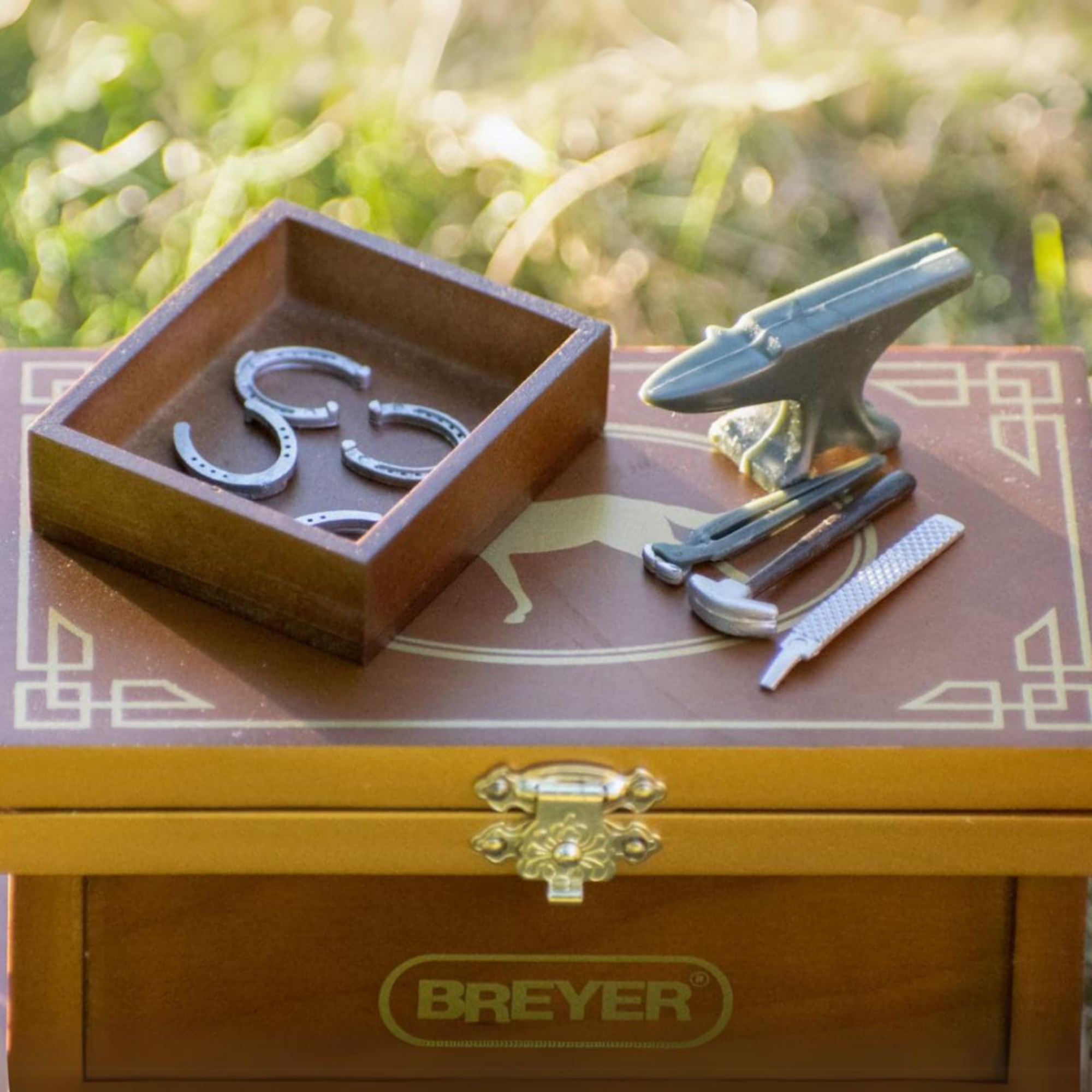 Breyer Horse Farrier Model Figure Accessories Upclose. Featuring a Wooden box with horseshoes and tools on a grassy background, with the Breyer brand.