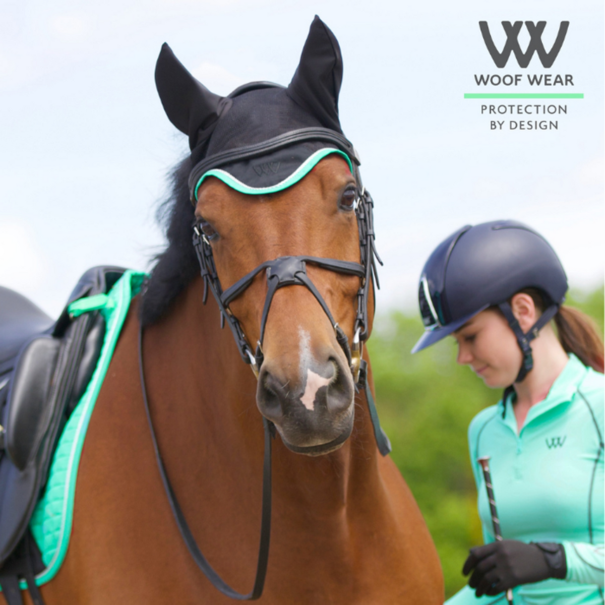 Girl holding a tacked up dressage horse wearing a Woof Wear Black & Mint Ergonomic Fly Veil with silver rope edging and mint binding.