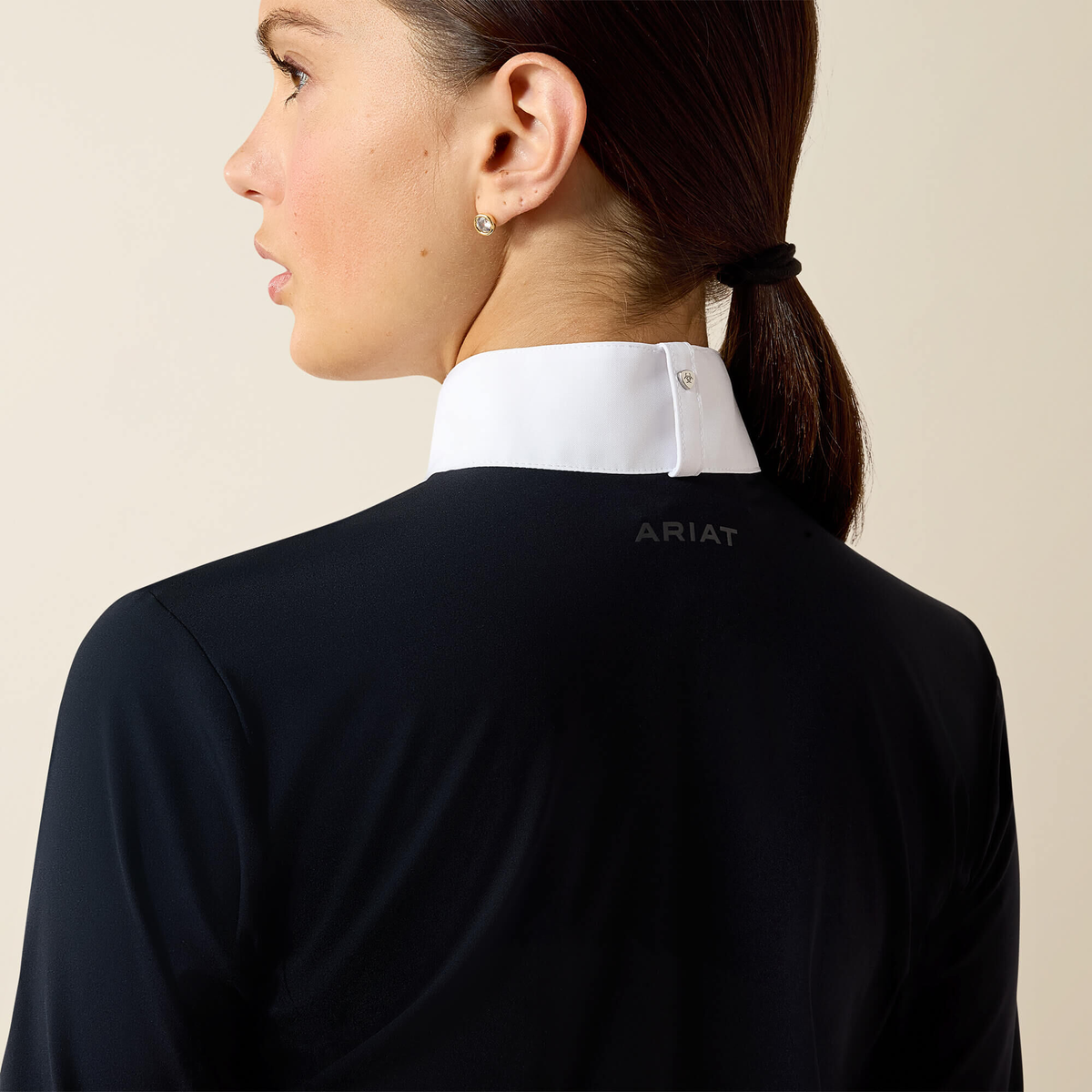Closeup back view of a woman wearing a navy Ariat SolVeil Long Sleeve Show Shirt with a white collar on a beige background .