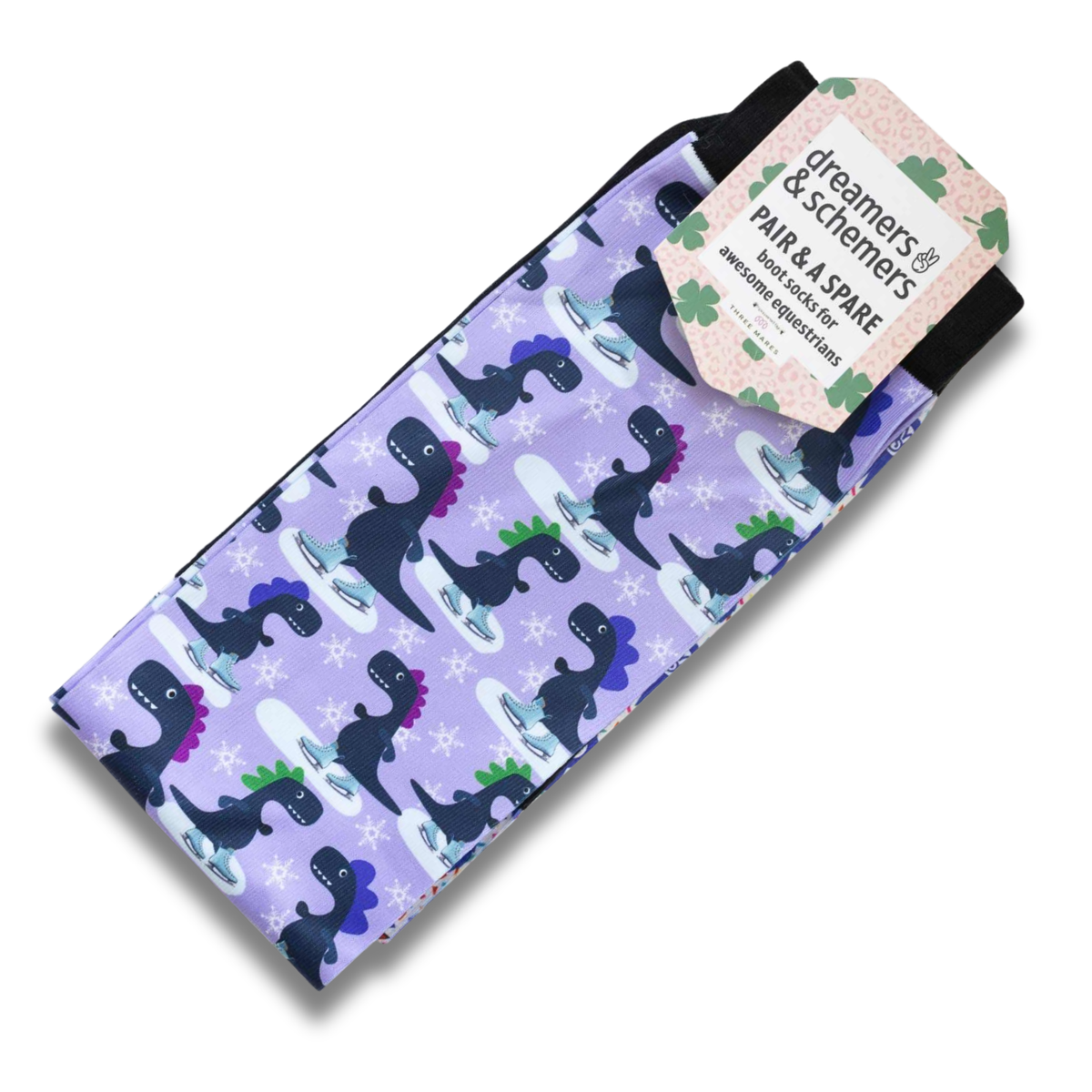 A pair of dreamers & schemers boot socks featuring a purple background with a pattern of dark blue dinosaurs wearing ice skates, accented with white snowflakes. A branded paper tag is attached to the top.