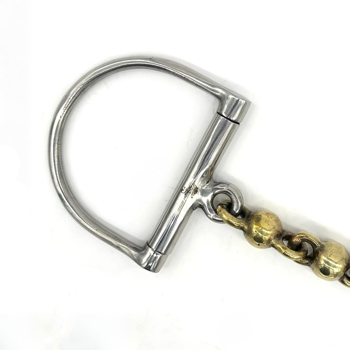 Closeup of the cheekpiece of a Jake Adams Equestrian Brass Waterford D bit on a white background.