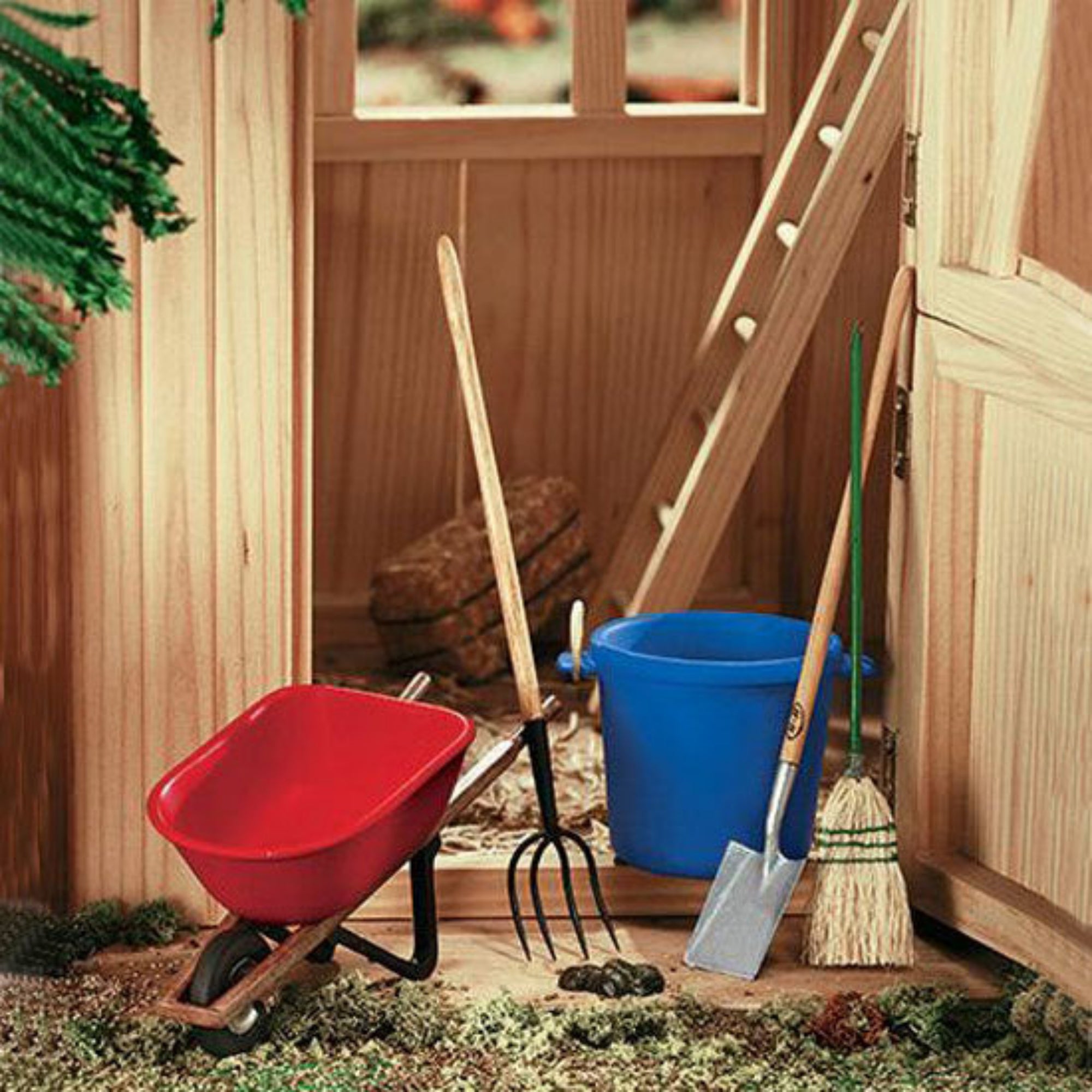 A Breyer Horse stable cleaning set including a broom, shovel, pitchfork, muck bucket, and wheelbarrow, with imitation manure, positioned in front of a wooden stable door.