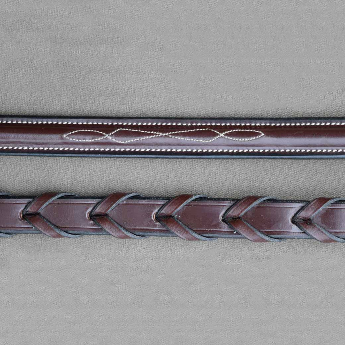A close-up of brown kl select leather horse reins with white fancy stitching.