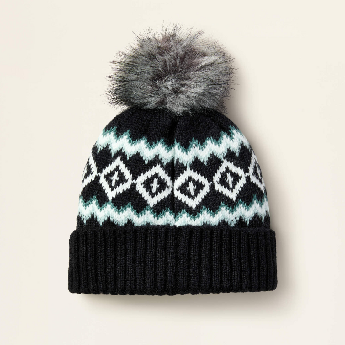 Black Ariat Bristol knit beanie with white and blue pattern and gray fur pom-pom on a light beige background
