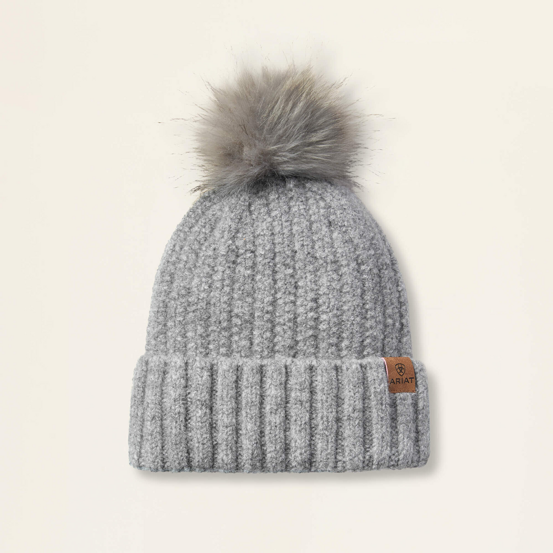 Slate colored Ariat Chiltion knit beanie with a faux fur pom-pom on a beige background