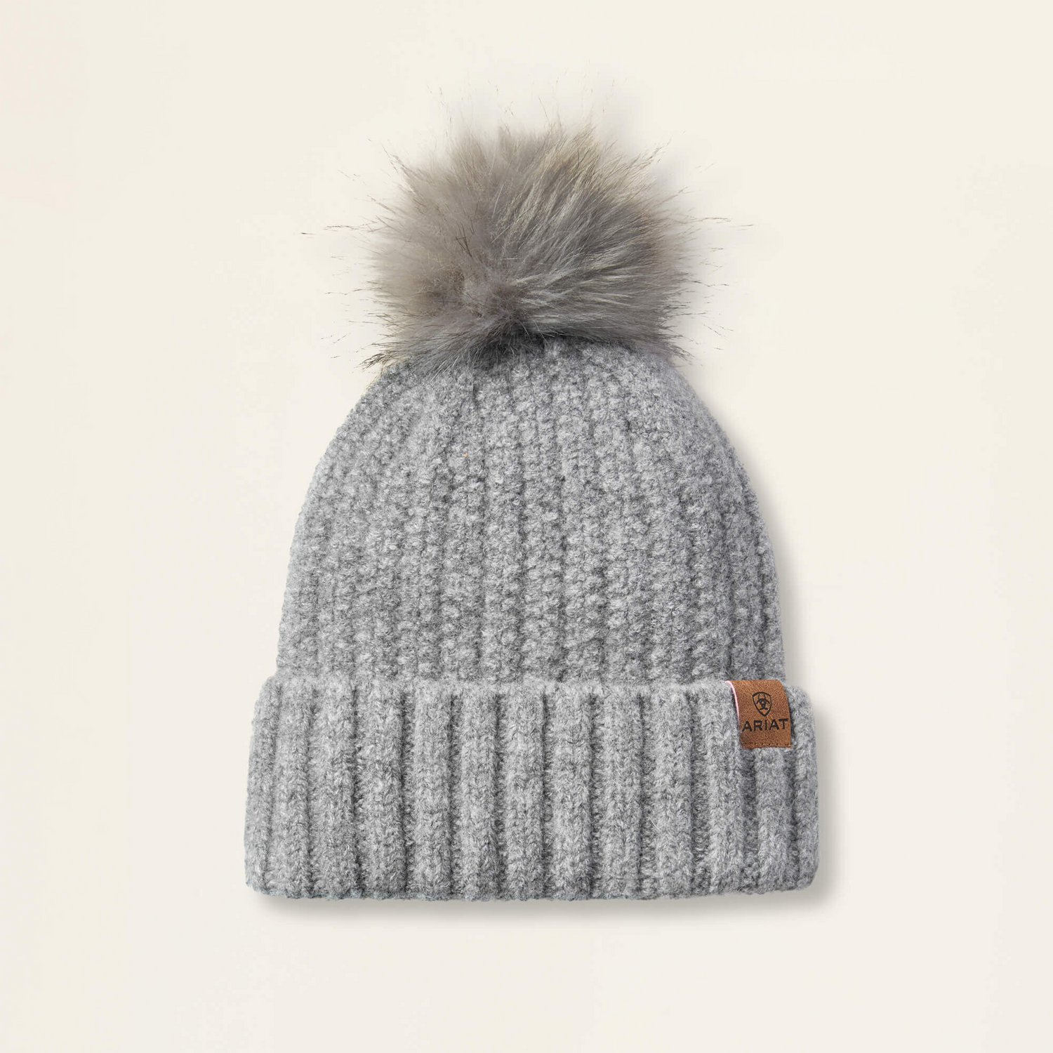Slate colored Ariat Chiltion knit beanie with a faux fur pom-pom on a beige background