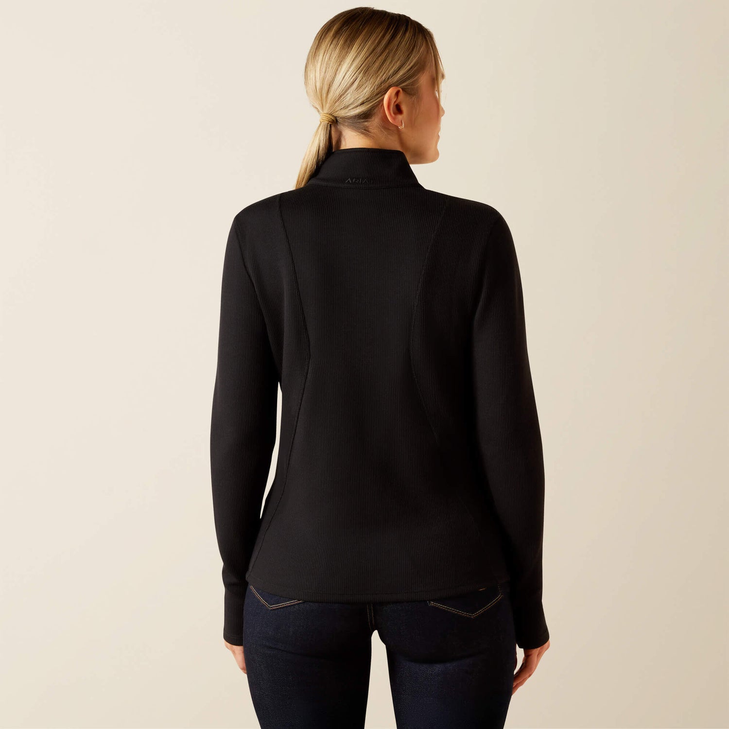 Woman wearing a black Ariat Lucent long-sleeve, quarter zip baselayer against a beige background