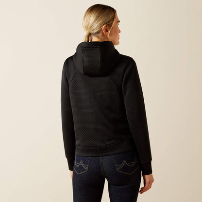 Blonde woman wearing a black patterned Ariat Radiance Full Zip jacke and dark jeans on a beige background