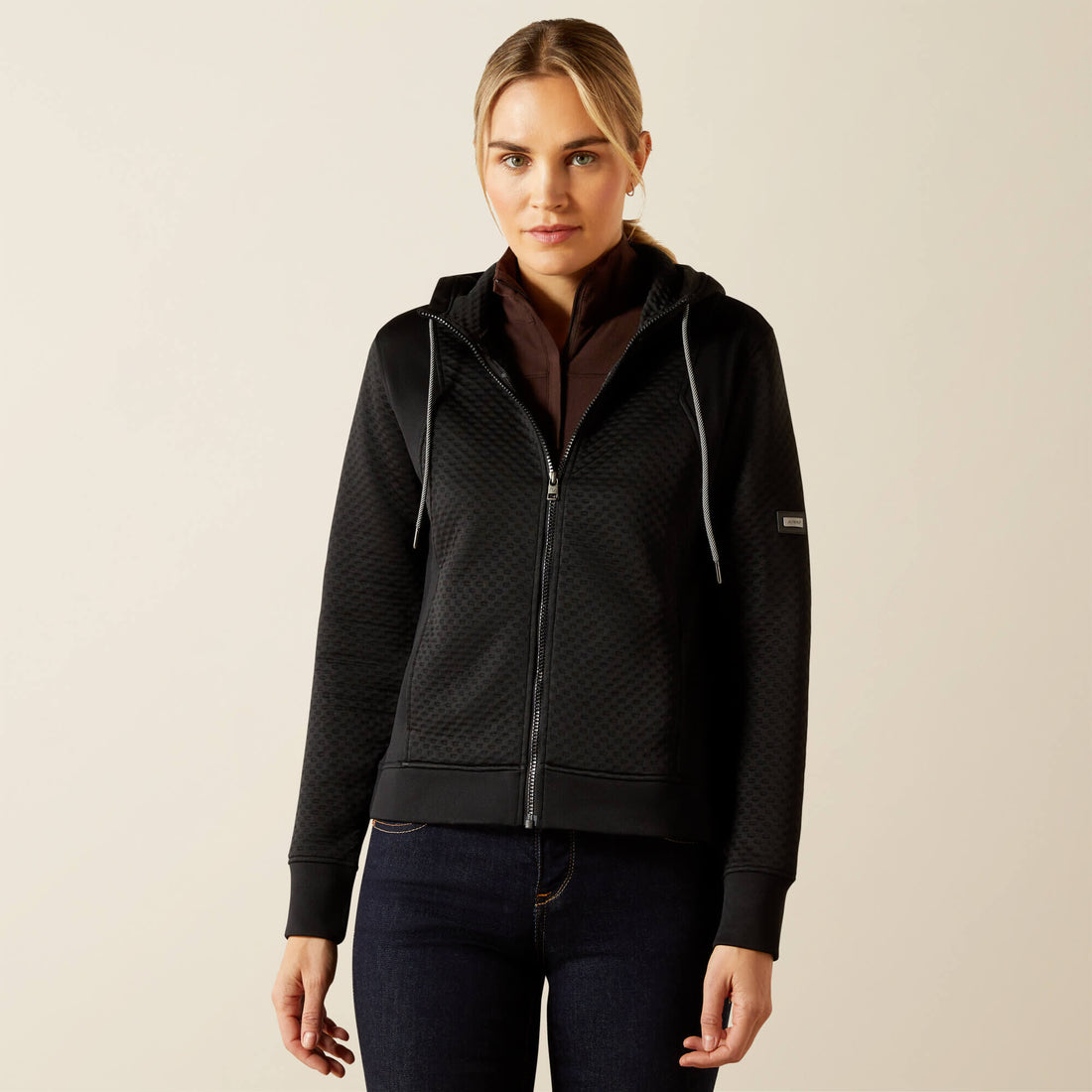 Woman wearing a black Ariat Radiance Full Zip quilted jacket on a beige background.