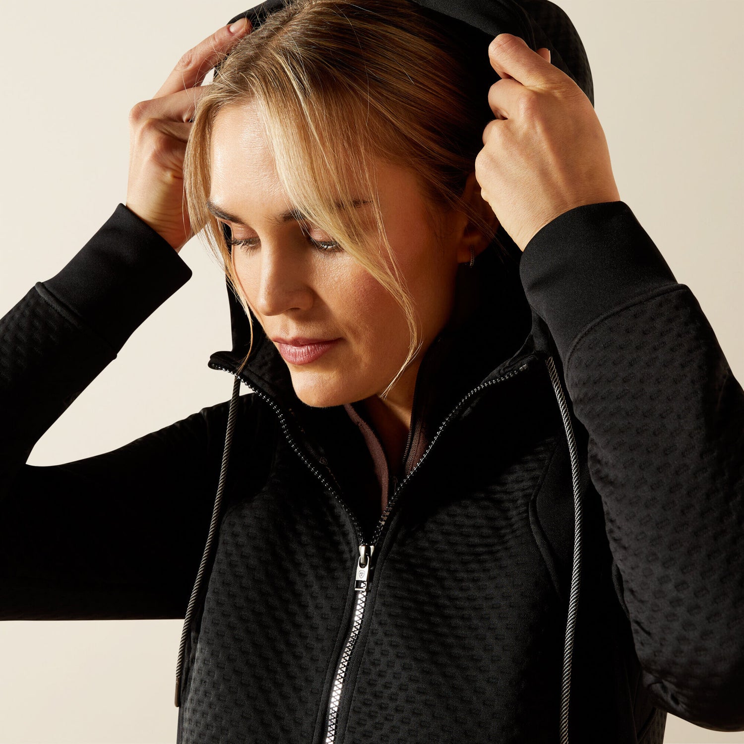 Woman wearing a black Ariat Radiance Full Zip  jacket with a textured pattern on a beige background