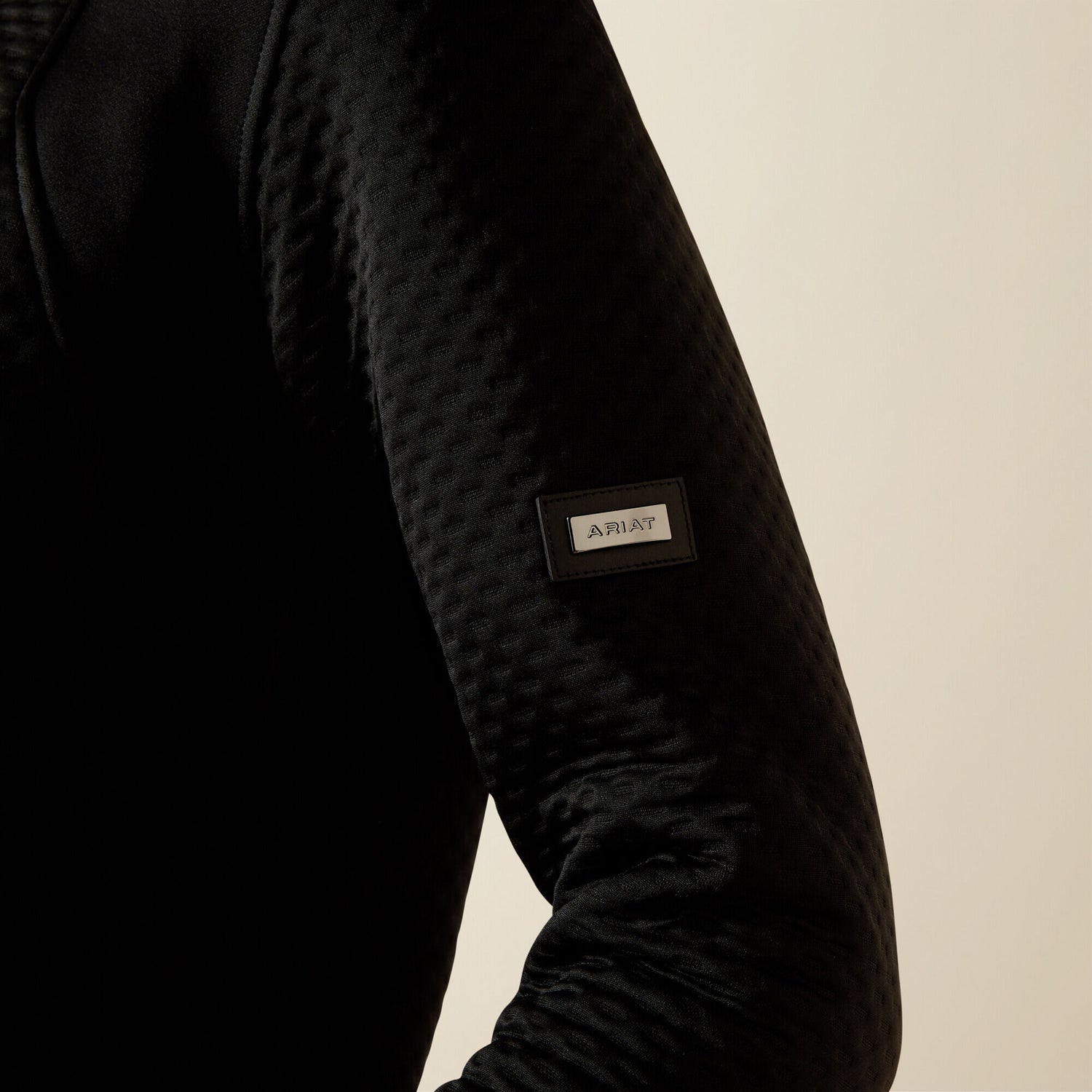 Ariat Radiance Full Zip black jacket sleeve with a brand label on a beige background