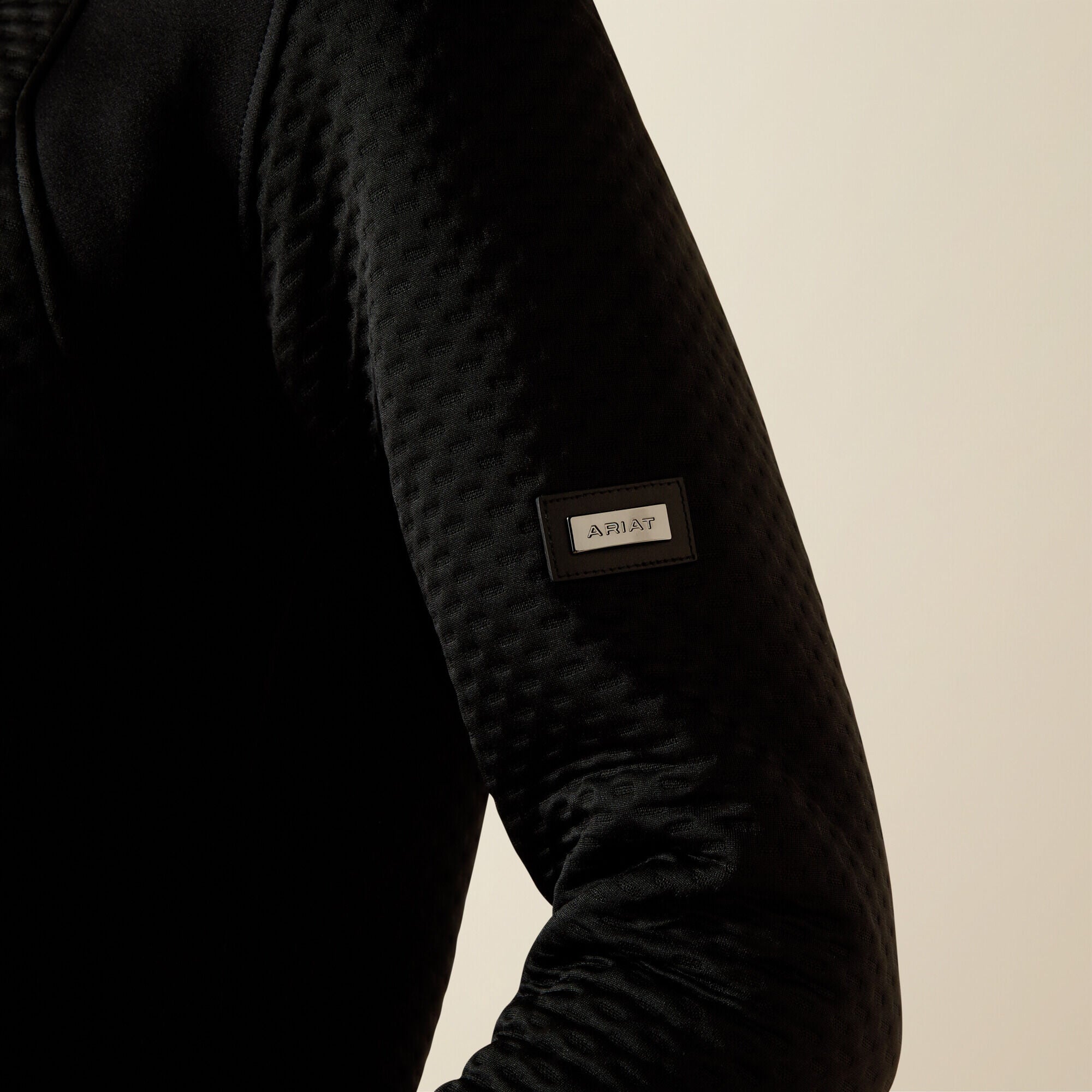 Ariat Radiance Full Zip black jacket sleeve with a brand label on a beige background