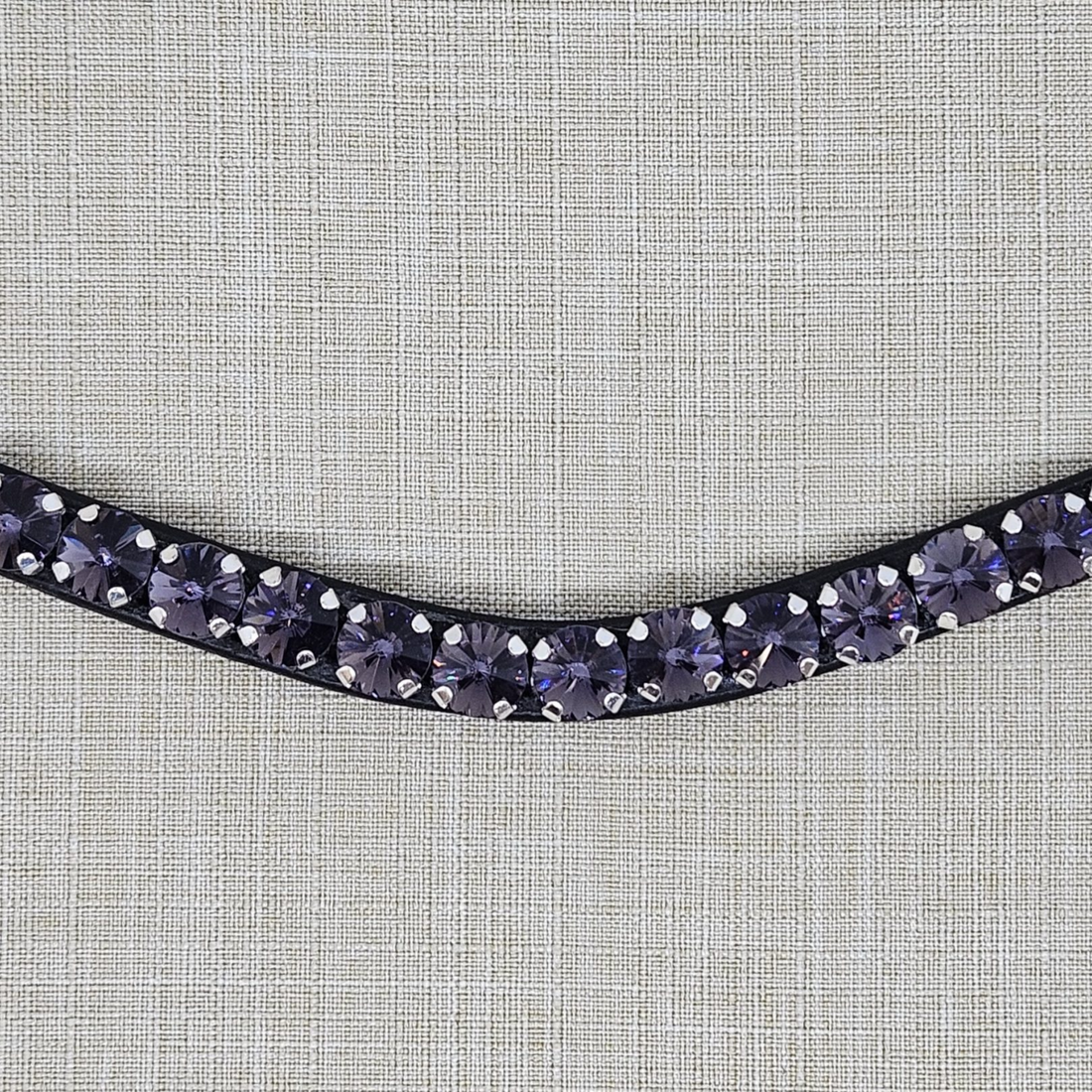Close up view of a Black leather browband with purple crystals on a textured gray background. Browband is from KL Select Red Barn. Purple Passion.