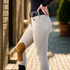 A person wearing Tan Tailored Sportsman Tech Breeches with clarino suede knee patches and a black quilted belt, standing outdoors.