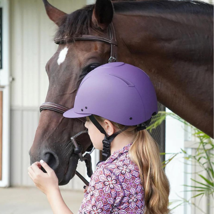 Girl holding and petting a horse while wearing a purple IRH Equi-Pro Deluxe Schooling Helmet with Sun Visor .  The back is visible.