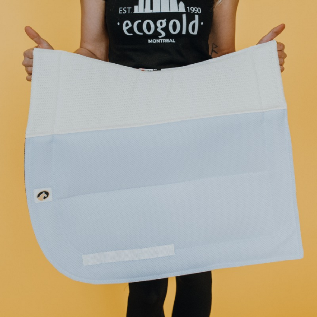 A person holding up an Ecogold Secure Pony Dressage Pad, which is white in color.