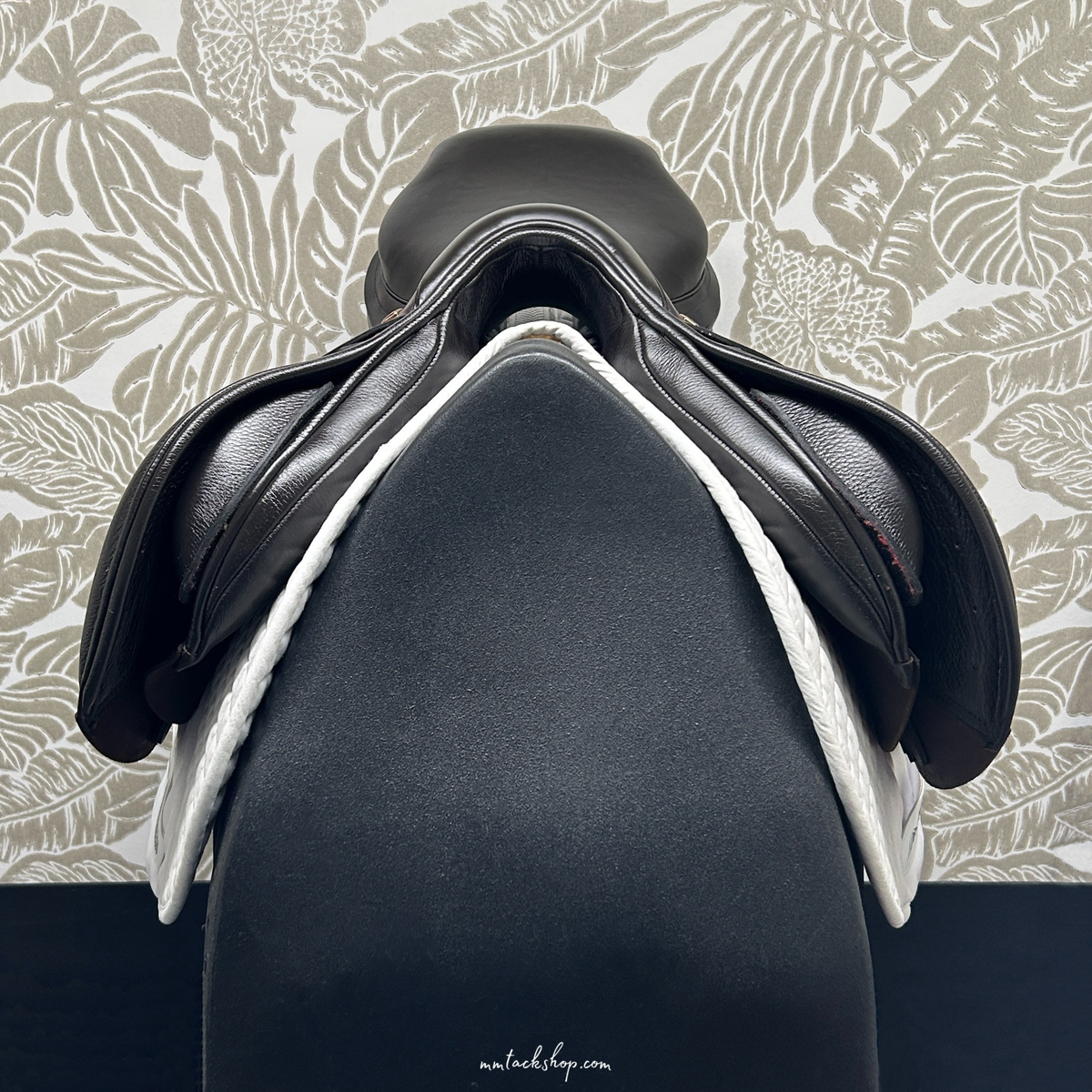 The front view of a demo 17.5",  dark Havana, flat forward, medium wide Albion jump saddle against a patterned background.