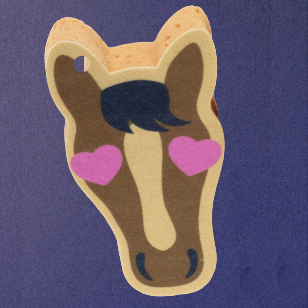Dreamers and Schemers Pony Love novely horse bath spong brown face, beige outline, black mane, and pink heart-shaped eyes, shown on a solid purple background.