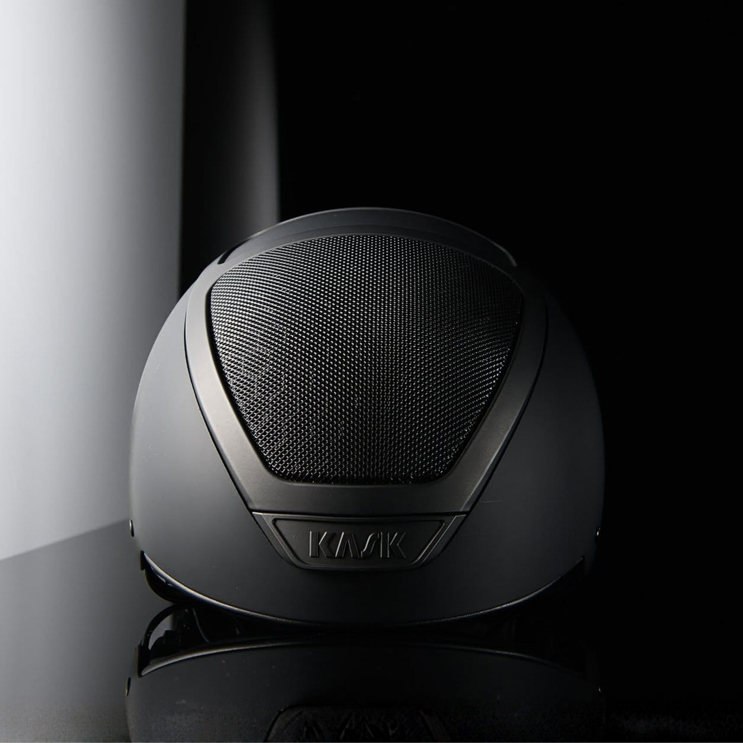 A matte black Kask Dogma cross country helmet shown from the front, resting on a reflective black surface against a dark studio background.