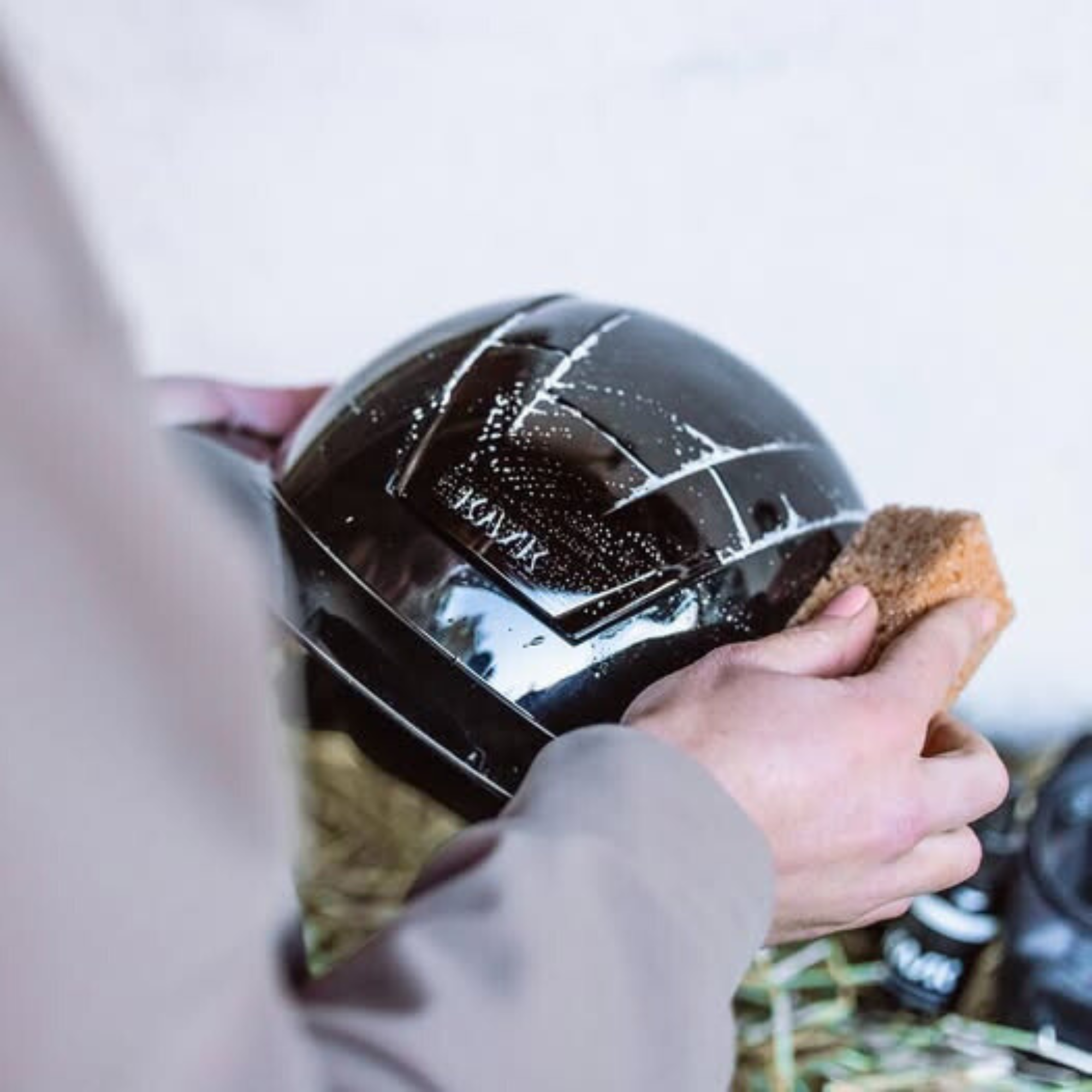 Person cleaning a black KASK helmet with KASKs Helmet Cleaning Kit sponge against a neutral background