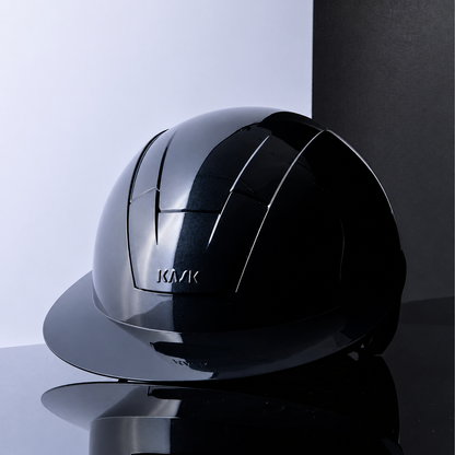 A glossy metallic navy KASK Kooki Lady riding helmet with a visor, displayed on a reflective black surface against a split white and dark gray studio background.