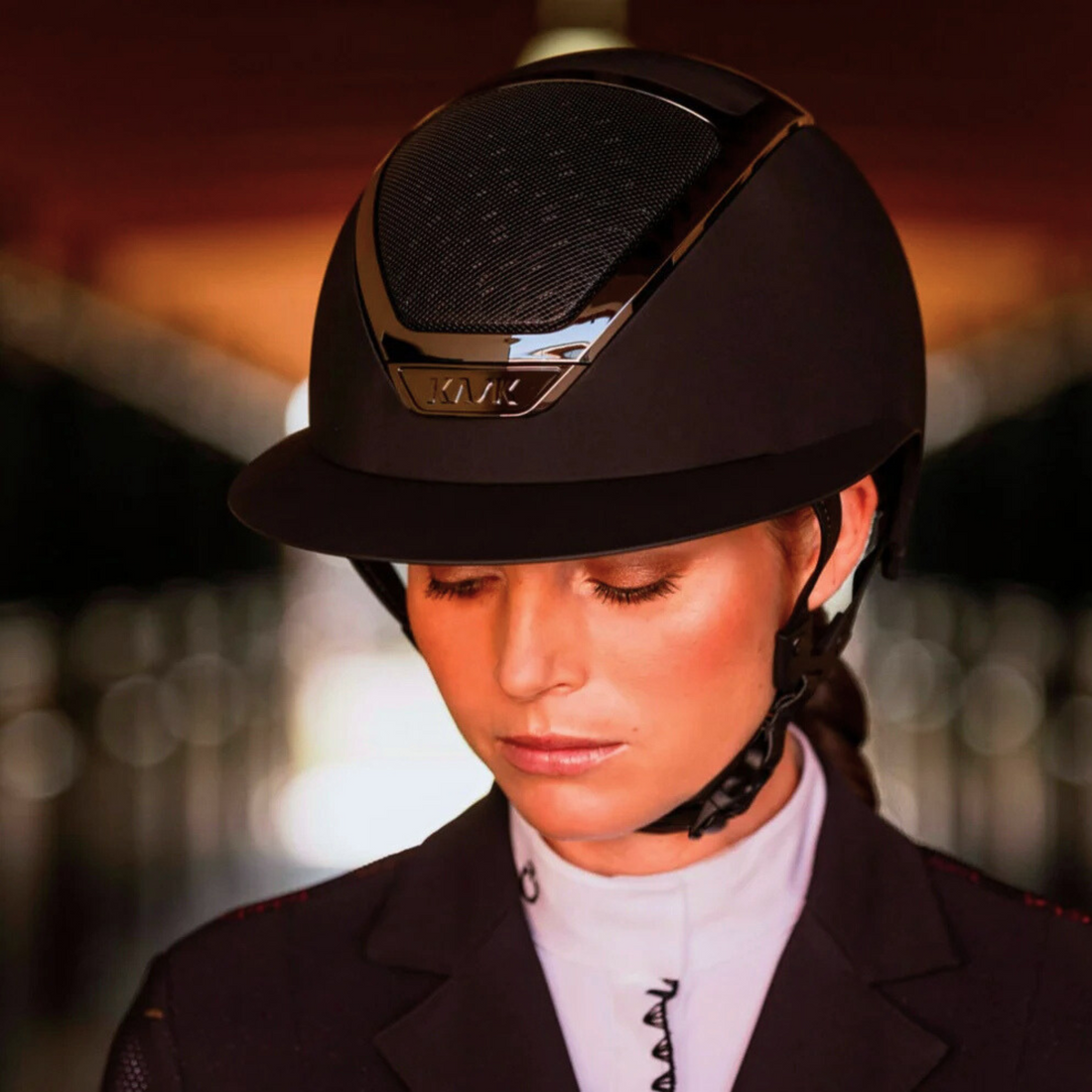 Female equestrian in show attire wearing a black KASK Star Lady Chrome riding helmet with a blurred background.