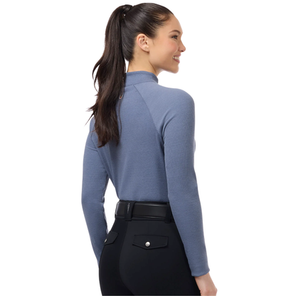 A woman with a dark ponytail is shown from the back wearing Kerrits Dusty Blue Align Textured Mock Neck Top, a slate blue long-sleeve mock top paired with black pants and a black belt, against a solid white background.