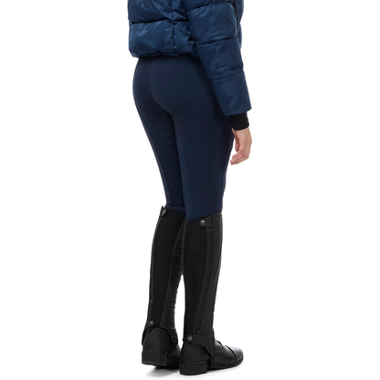 Rear three-quarter view of a model wearing nightfall colored Kerrits Fusion II Full Leg Equestrian Clinic Breeches, a navy quilted puffer jacket, and black equestrian riding boots against a white background.