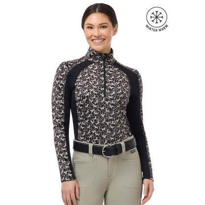 A woman modeling a long-sleeve Kerrits Traverse quarter zip fleece tech top with a beige horse pattern and solid black ribbed sides &amp; under sleeves paired with beige riding pants. A &