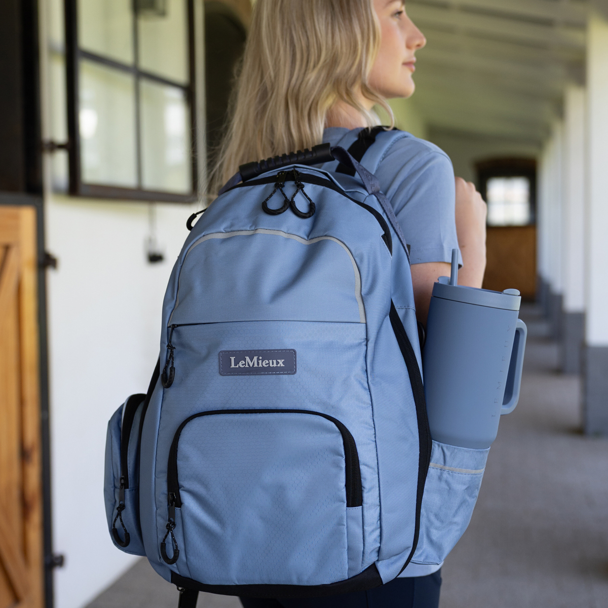 Person wearing a powder blue LeMieux Pro Rusksack with LeMieux logo, holding a matching water bottle.