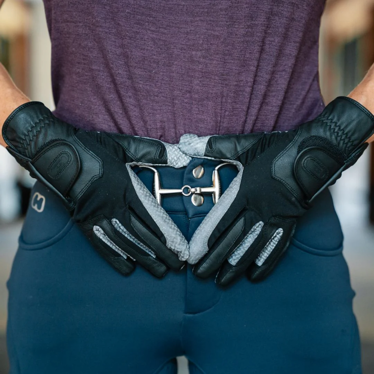 Person wearing black gloves with a silver buckle, standing against a blurred background.