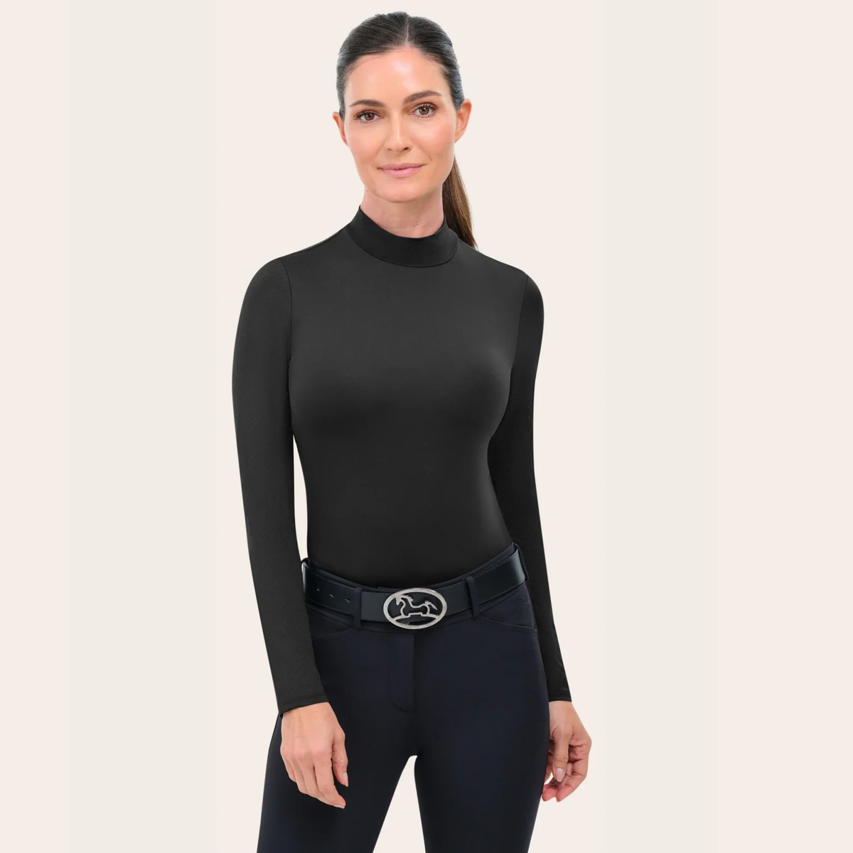 Woman wearing a black RJ Classics long-sleeve top and black riding breeches with a belt on a beige background.