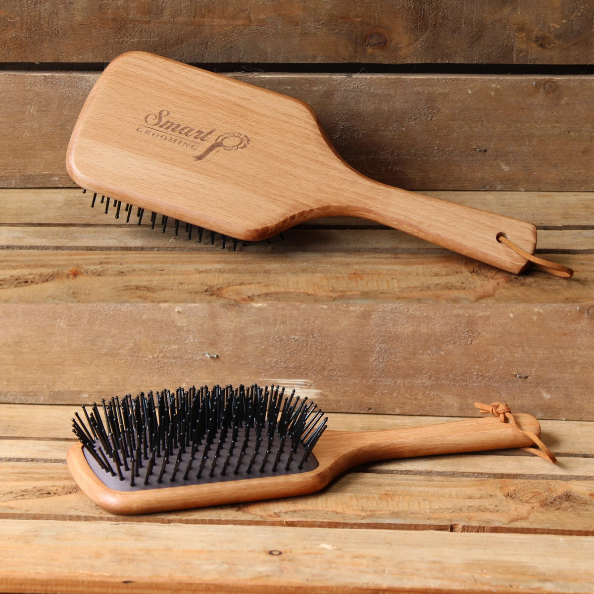 Two wooden backed, black bristled Smart Grooming Large mane &amp; tail brushes are displayed on a rustic wooden plank surface. The top brush is shown from the back, featuring a branded handle with the brand name &