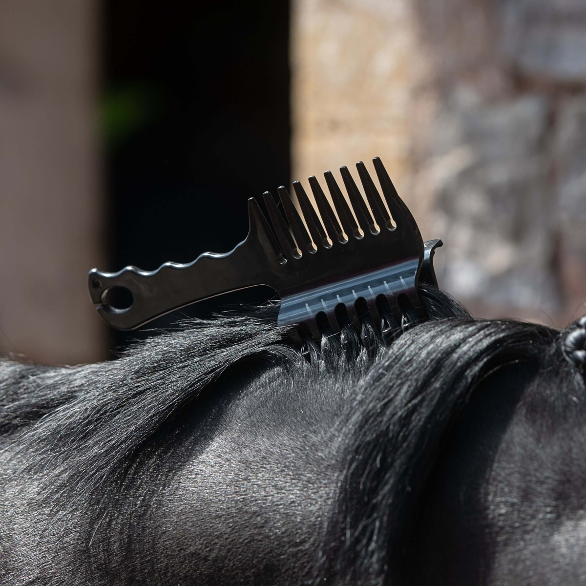 A close-up of a black Smart Grooming Perfect Plaits horse comb clipped into a dark horses mane.