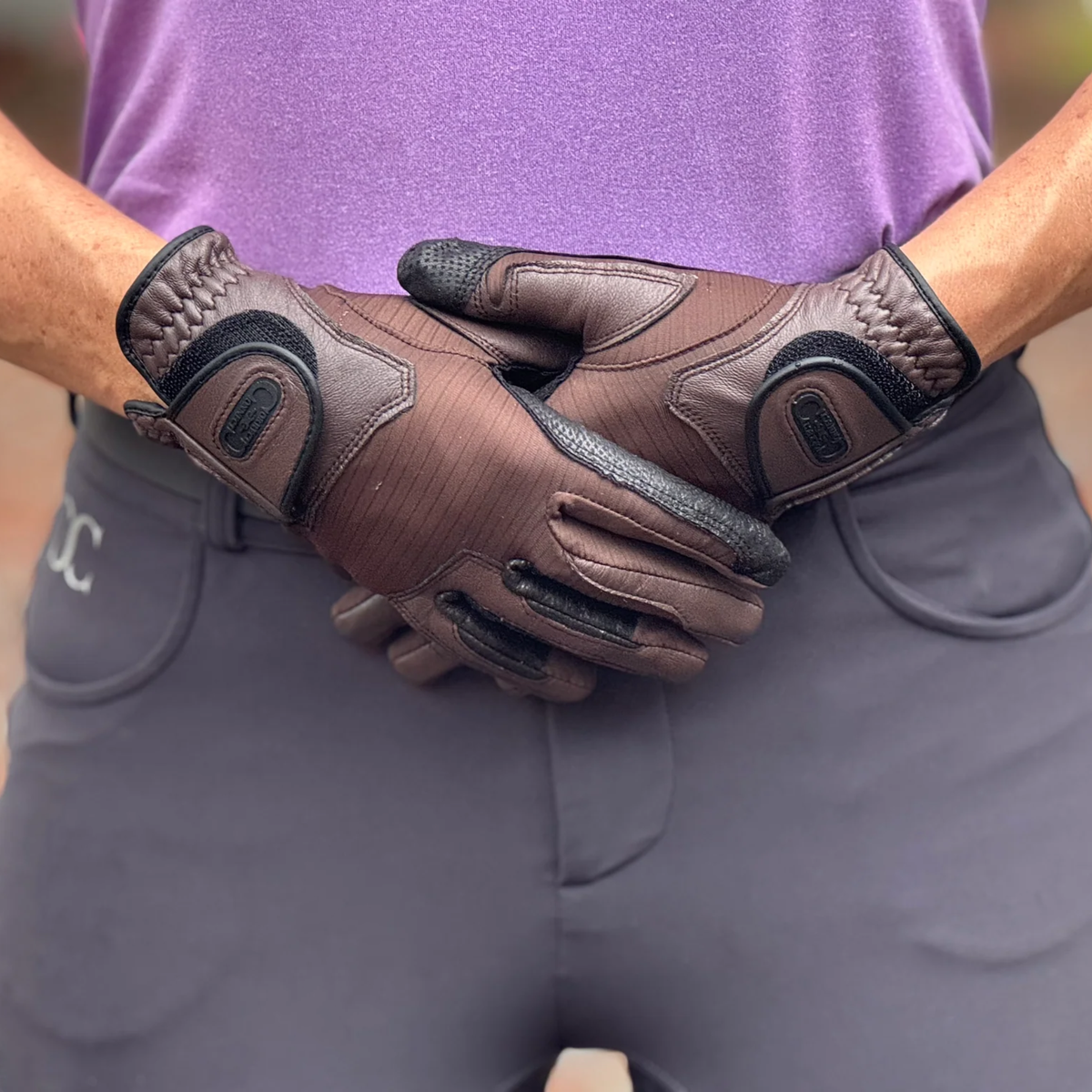 Person wearing brown gloves with black accents, against a blurred background.