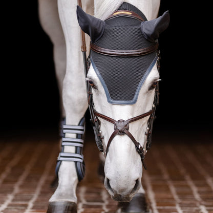 A horse wearing an EquiFit Silent Fit Ear Bonnet, which is black with brown straps and has foam lining.
