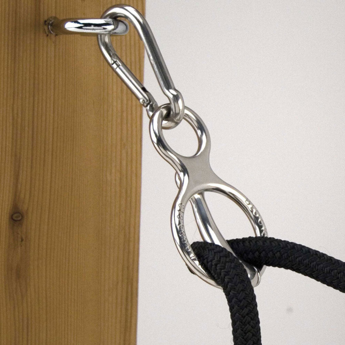 A silver-colored metal tie ring mounted on a wooden post, with a black lead rope attached to it.