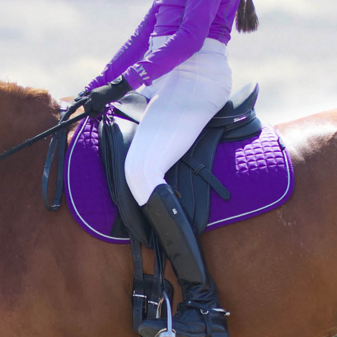 A person riding a horse wearing a purple Woof Wear Dressage Saddle Pad.