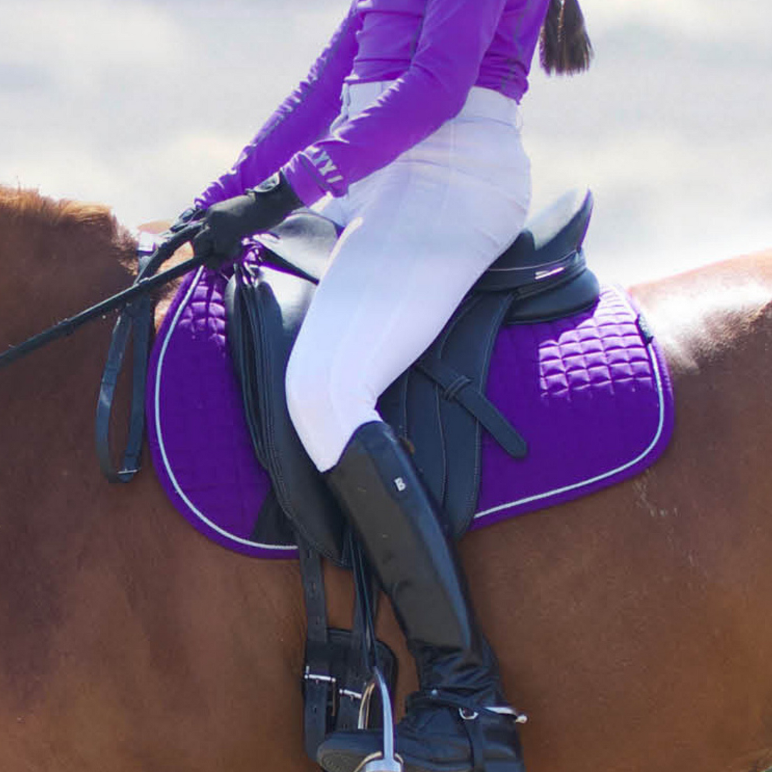 A person riding a horse wearing a purple Woof Wear Dressage Saddle Pad.